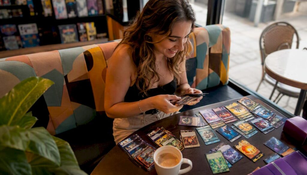 1785702933688JeunefemmetriantdeckcartesTCGencafe JM Cards Une jeune femme assise dans un café en train de trier son deck de cartes TCG