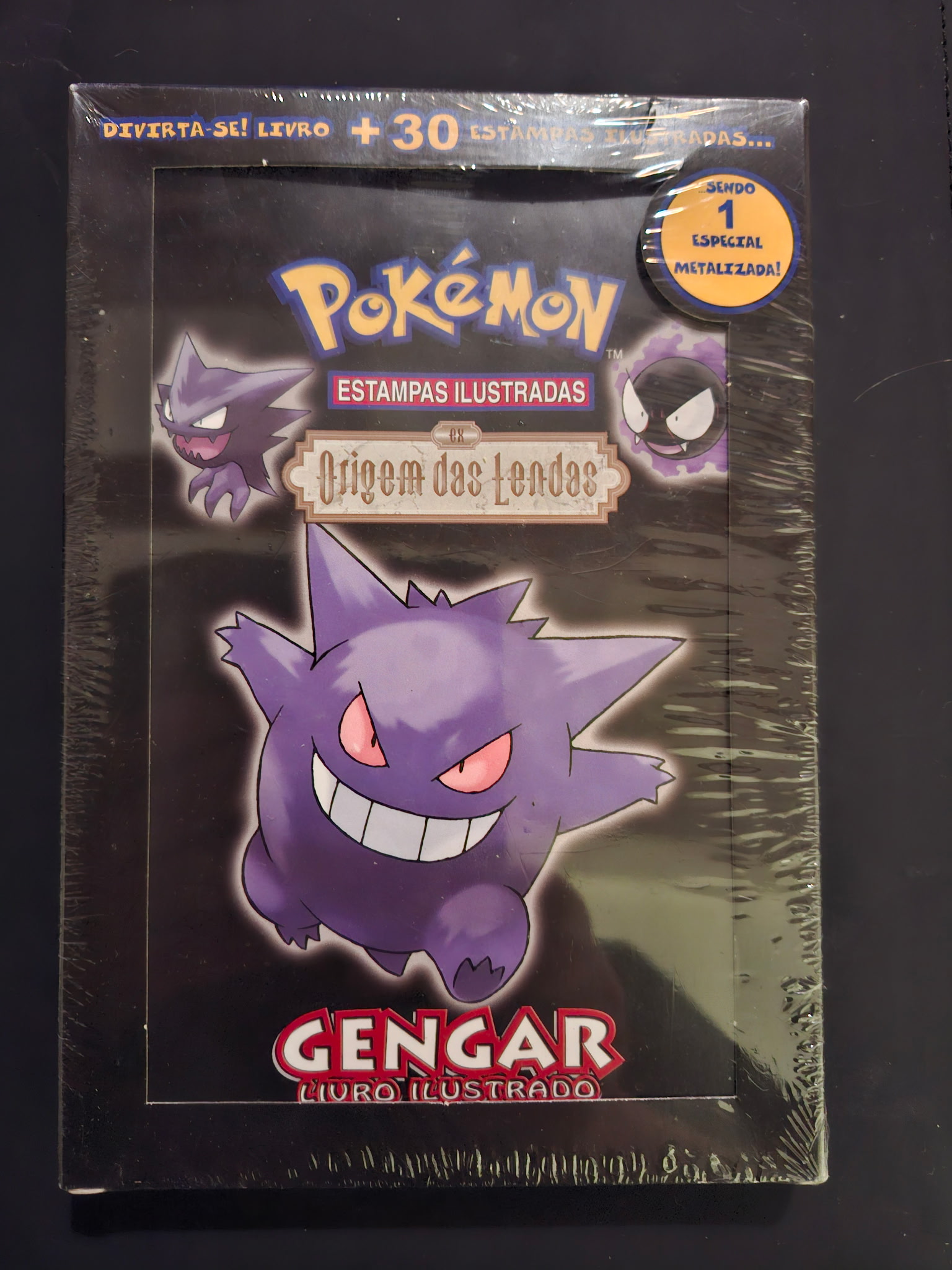 20260828013427 JM Cards Front cover of a Pokémon Estampas Ilustradas book featuring a purple Gengar illustration on a dark background