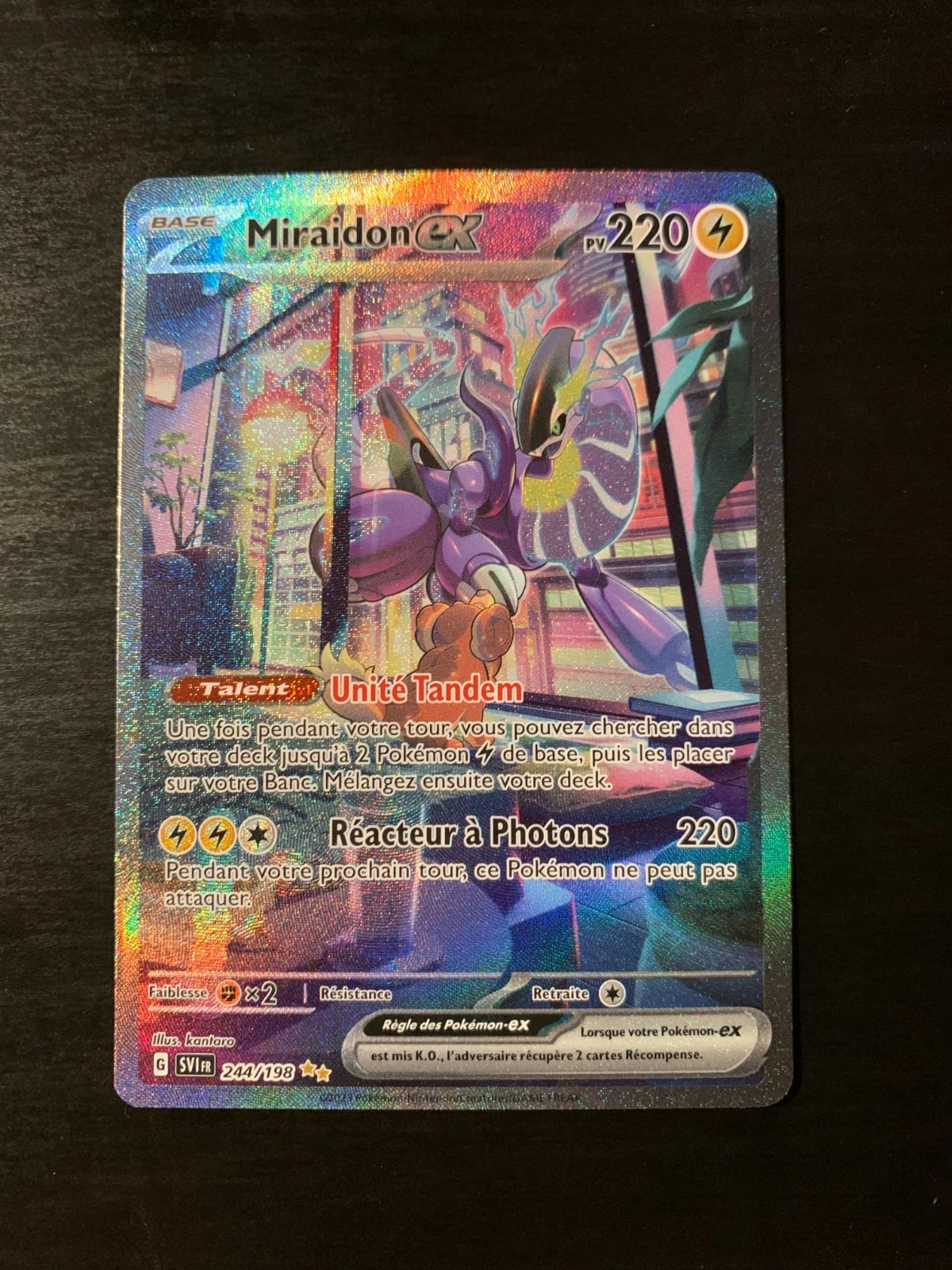 Holographic Miraidon ex Pokémon card with neon city artwork, 220 HP, and Tandem Unite move (French text).