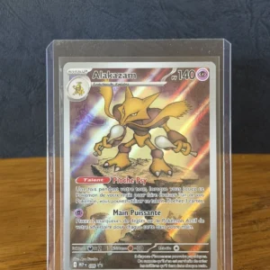 Pokémon Alakazam trading card in a clear protective case on a wooden surface, holographic border visible